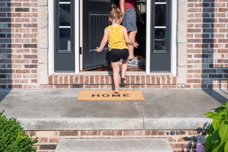 Barefoot little girl entering the front door of a home with a we