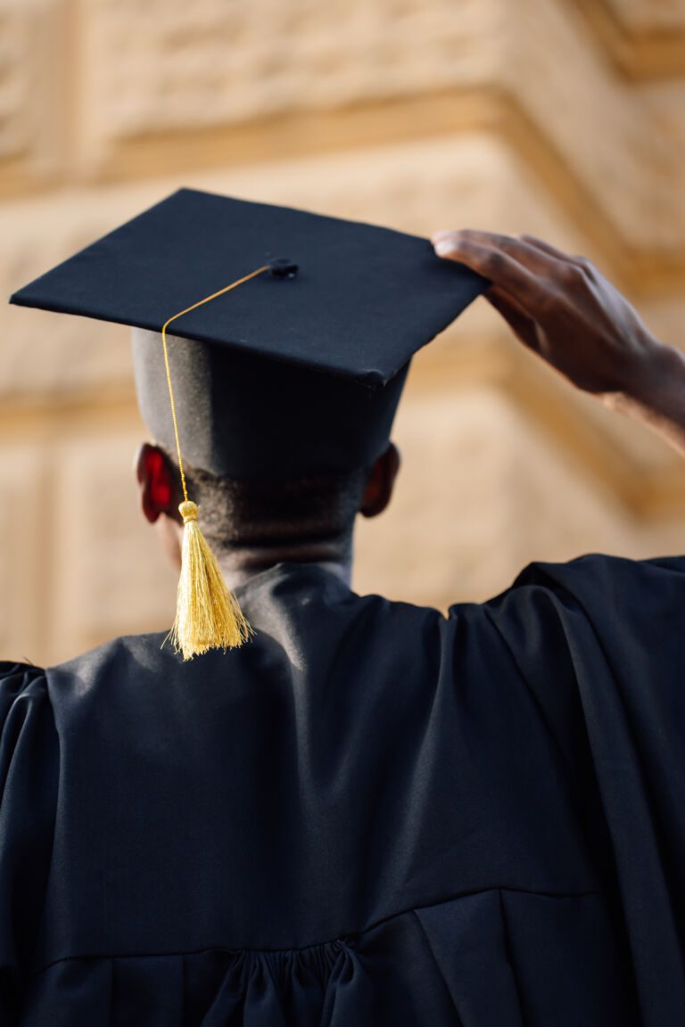 Portrait closeup of black student in graduation mantle and hat standing with back outdoors and looking up at building. Employment, graduate from university, start in life, thoughts about future
